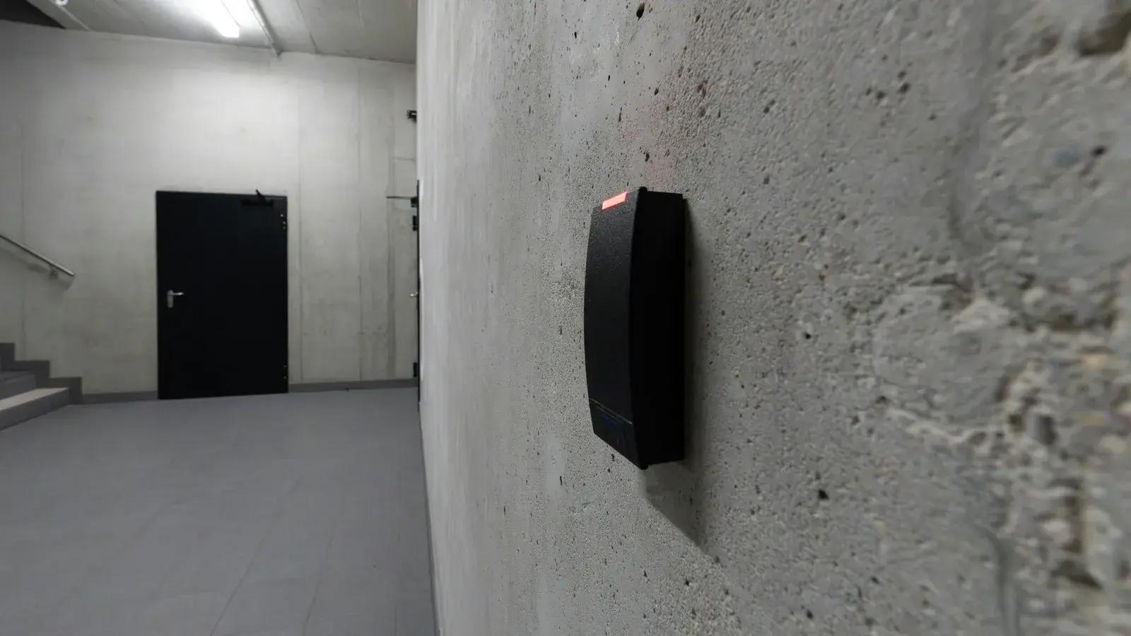 Kartenleser einer Zutrittskontrolle an der Betonwand neben einer verschlossenen Stahltür
