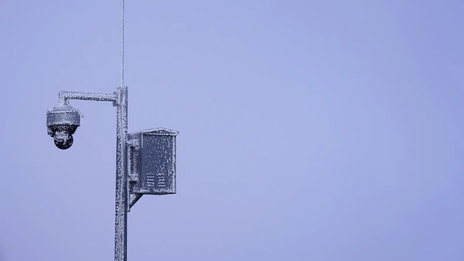 Überwachungskamera mit Schaltkasten an einem Mast vor winterlichem Himmel